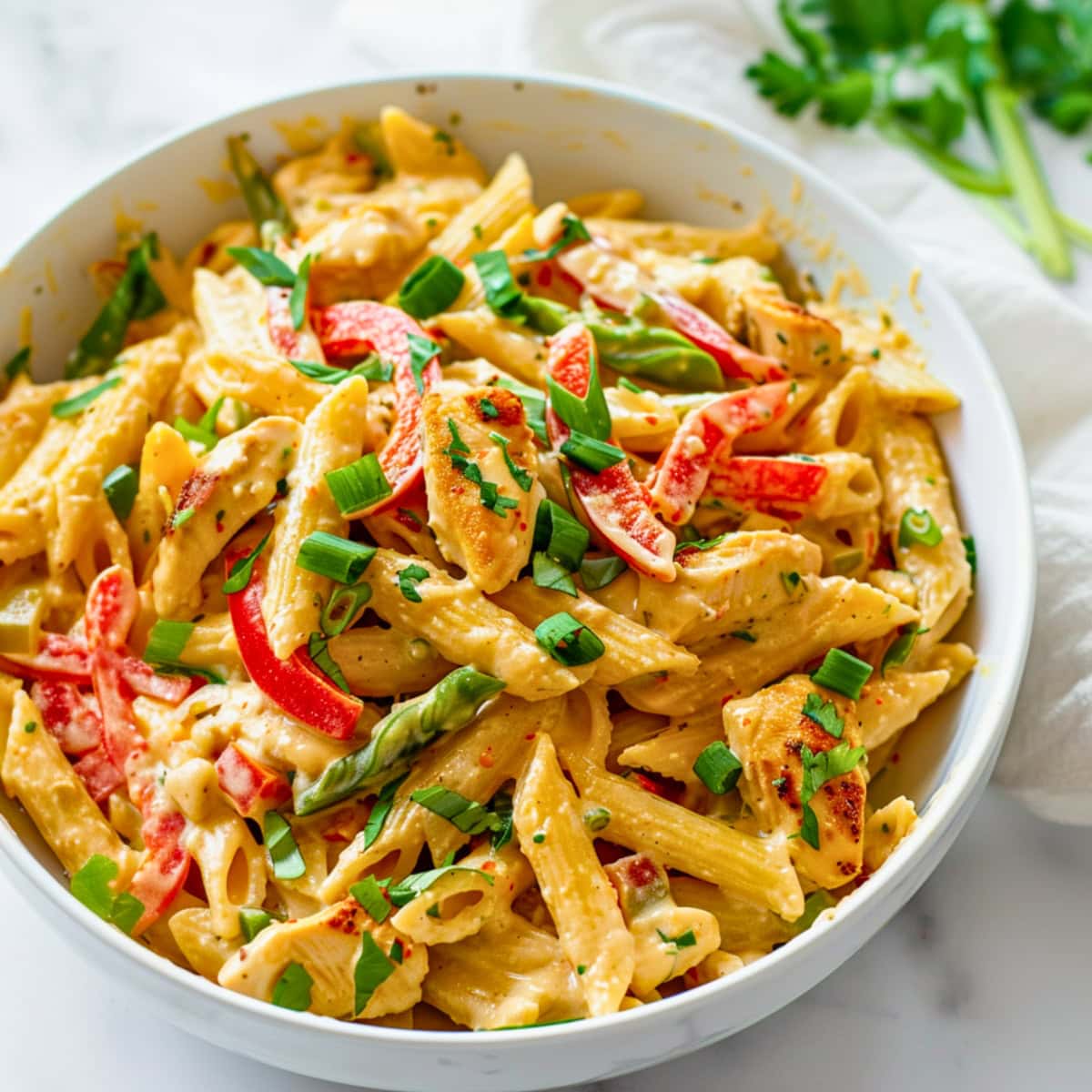 Bowl of creamy pasta with bell pepper and chicken breast, garnished with chopped green onions.