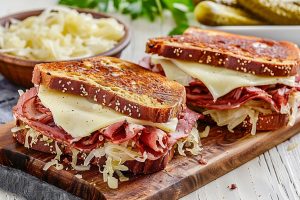 Two servings of reuben sandwich on a wooden chopping board.