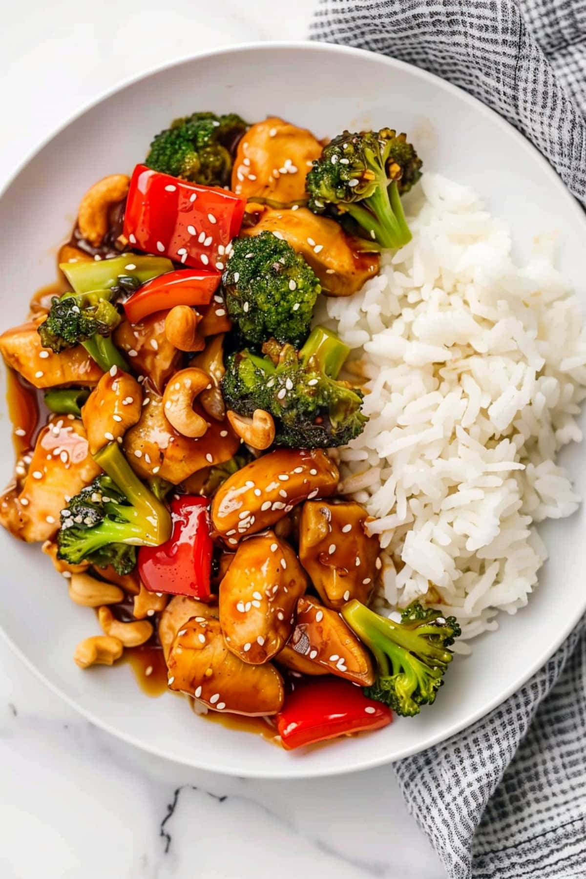 Teriyaki chicken and rice with vegetables and nuts in a white plate.