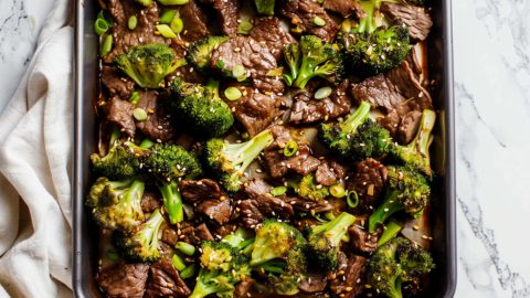 Top view of sheet pan beef and broccoli on a white marble table.