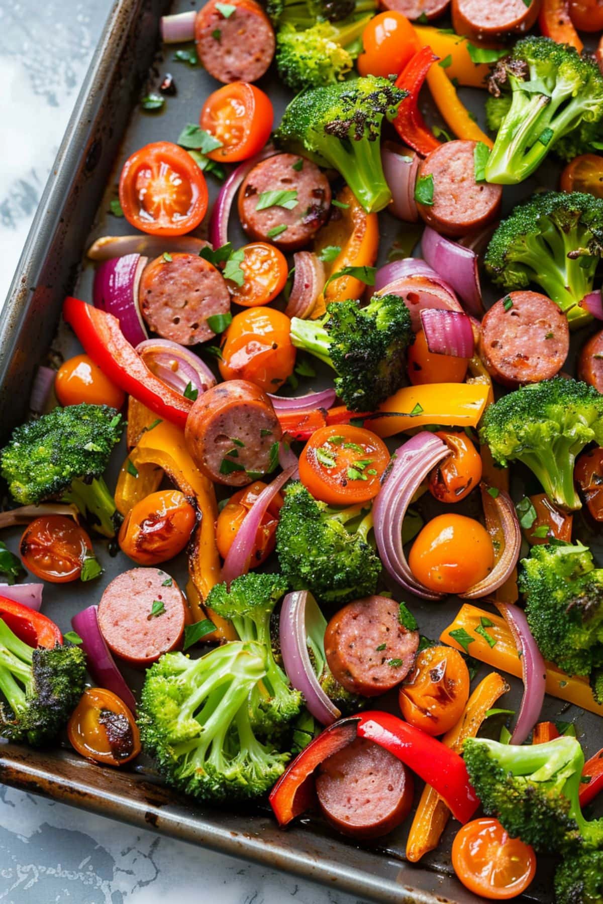 Sheet Pan Sausage and Veggies featuring bell peppers, broccoli florets, sliced red onion and cherry tomatoes tossed in olive oil and spices
