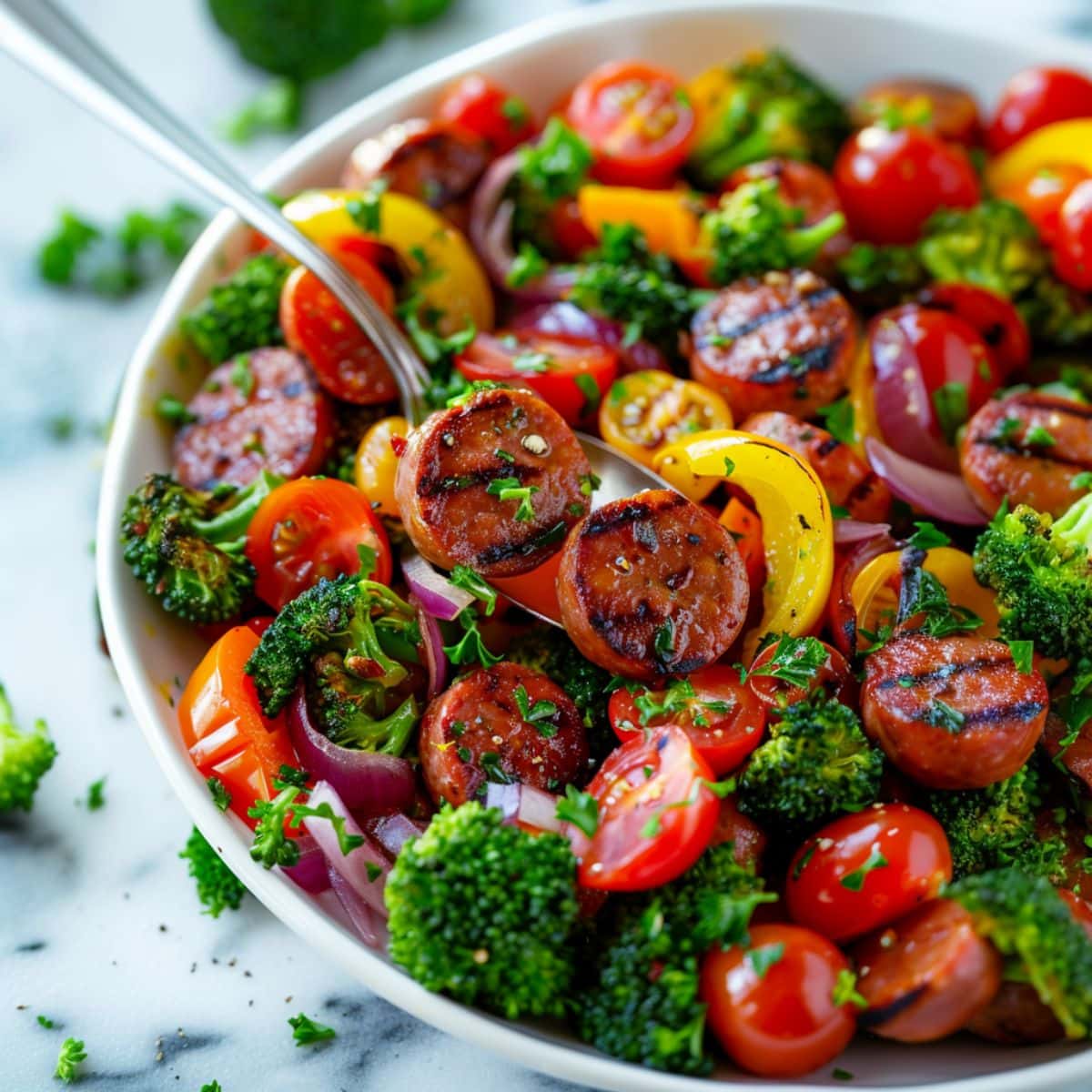 Sheet pan sausage and veggies served in a white bowl.