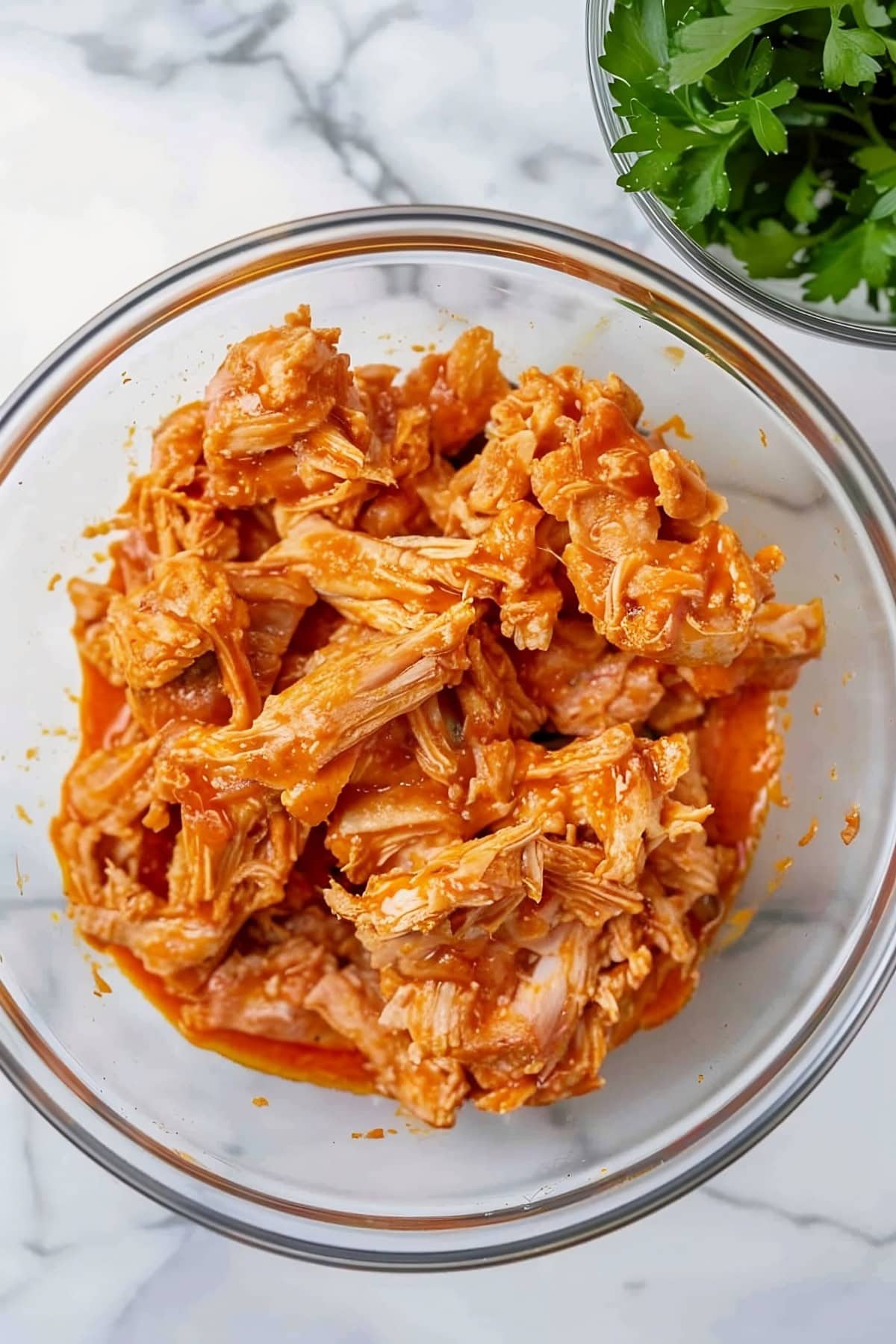 A glass bowl filled with shredded chicken and buffalo sauce.