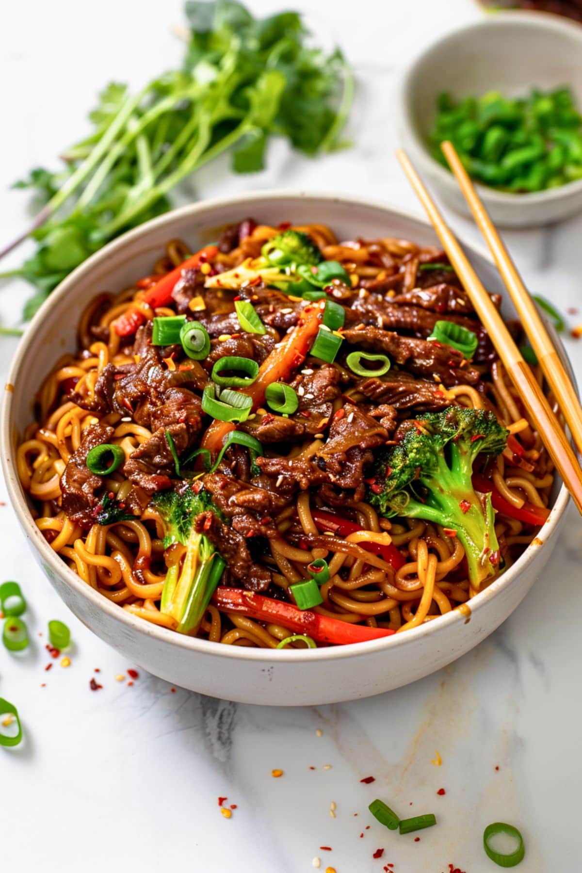 Sticky beef noodles with egg noodles, stir fired sliced thinly crispy sirloin steak, broccoli florets, sliced red bell pepper coated in thick and sticky sauce egg noodles served in a white bowl. 