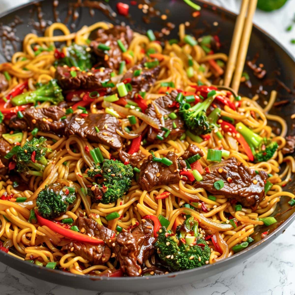 Sticky beef noodles with egg noodles, stir fired sliced thinly crispy sirloin steak, broccoli florets, sliced red bell pepper coated in thick and sticky sauce tossed in a wok pan.