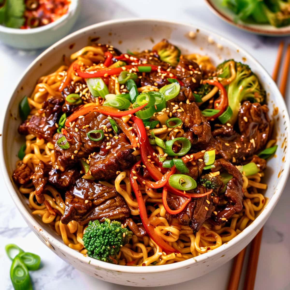 Bowl serving of sticky beef noodles with beef, broccoli florets, red bell pepper strips and egg noodles.