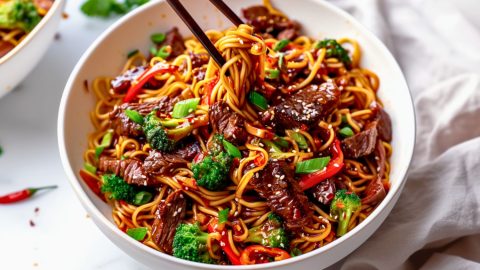 Sticky beef noodles served in a white bowl, chopstick lifting the noodles.