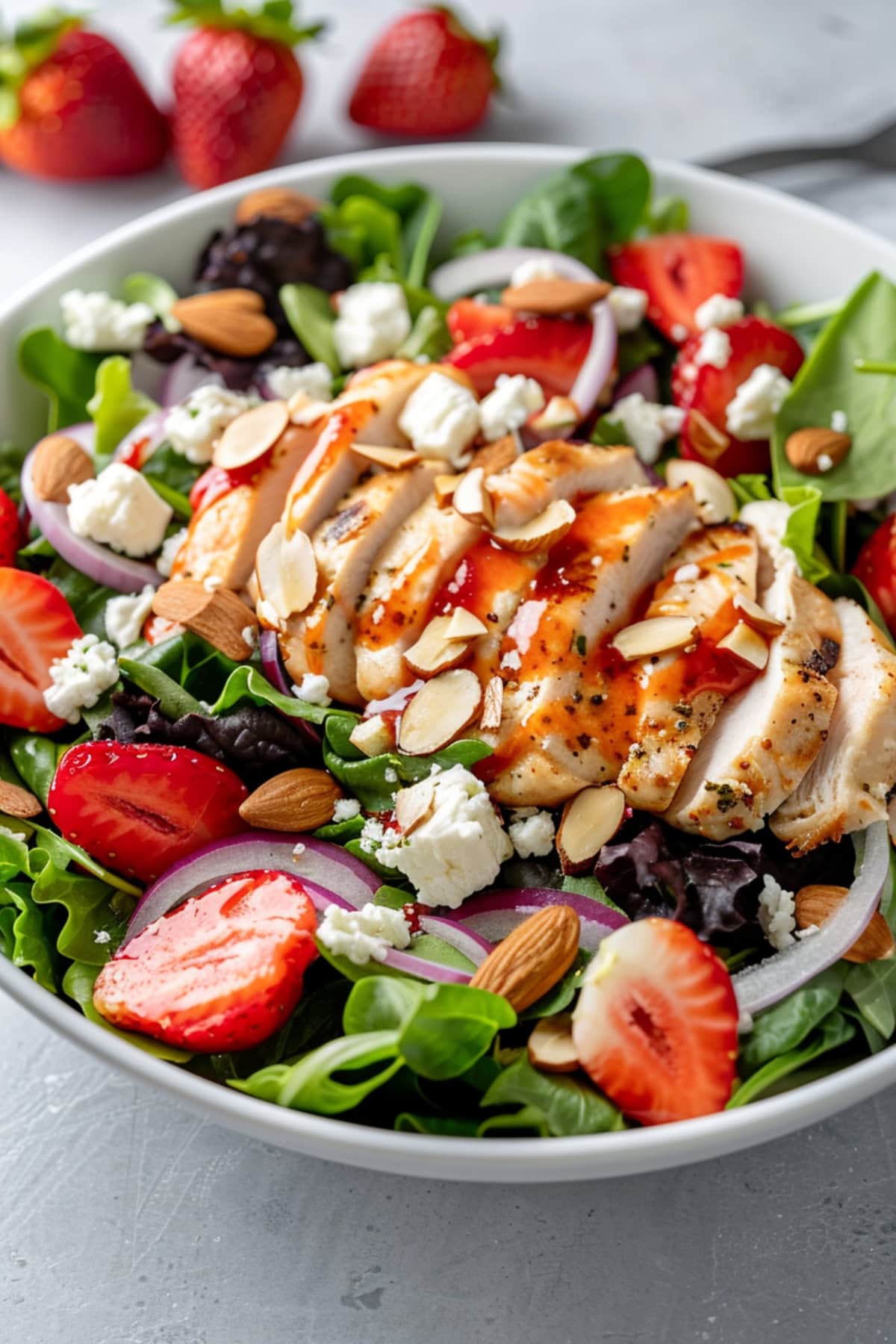 Strawberry chicken salad served in a white bowl drizzled with strawberry balsamic dressing. 