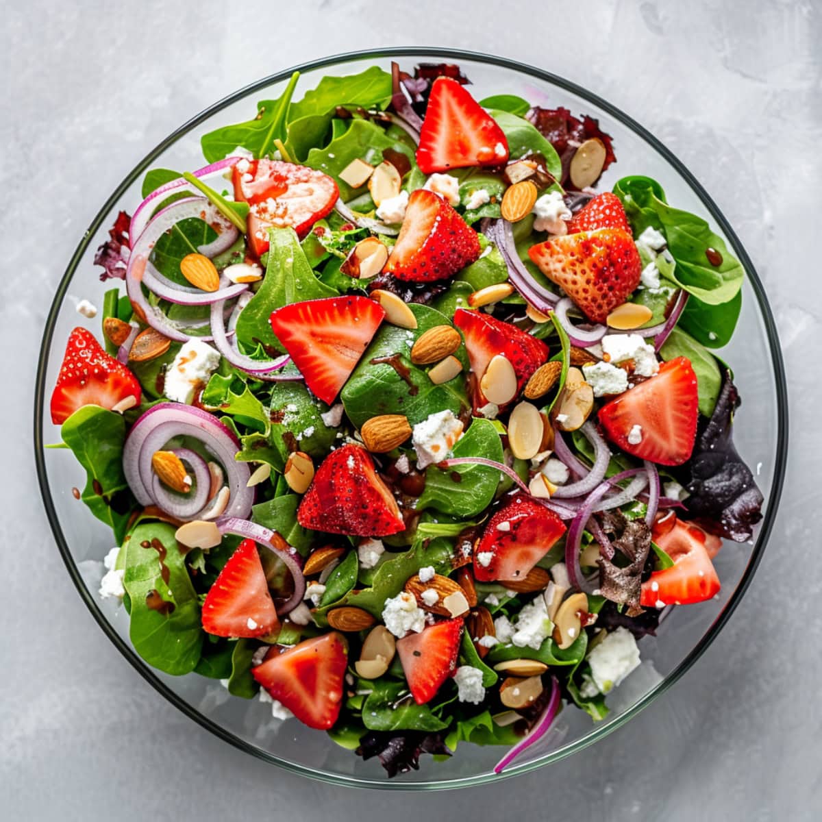 Mixed greens, sliced strawberries, crumbled feta cheese and sliced almonds in a large glass bowl. 