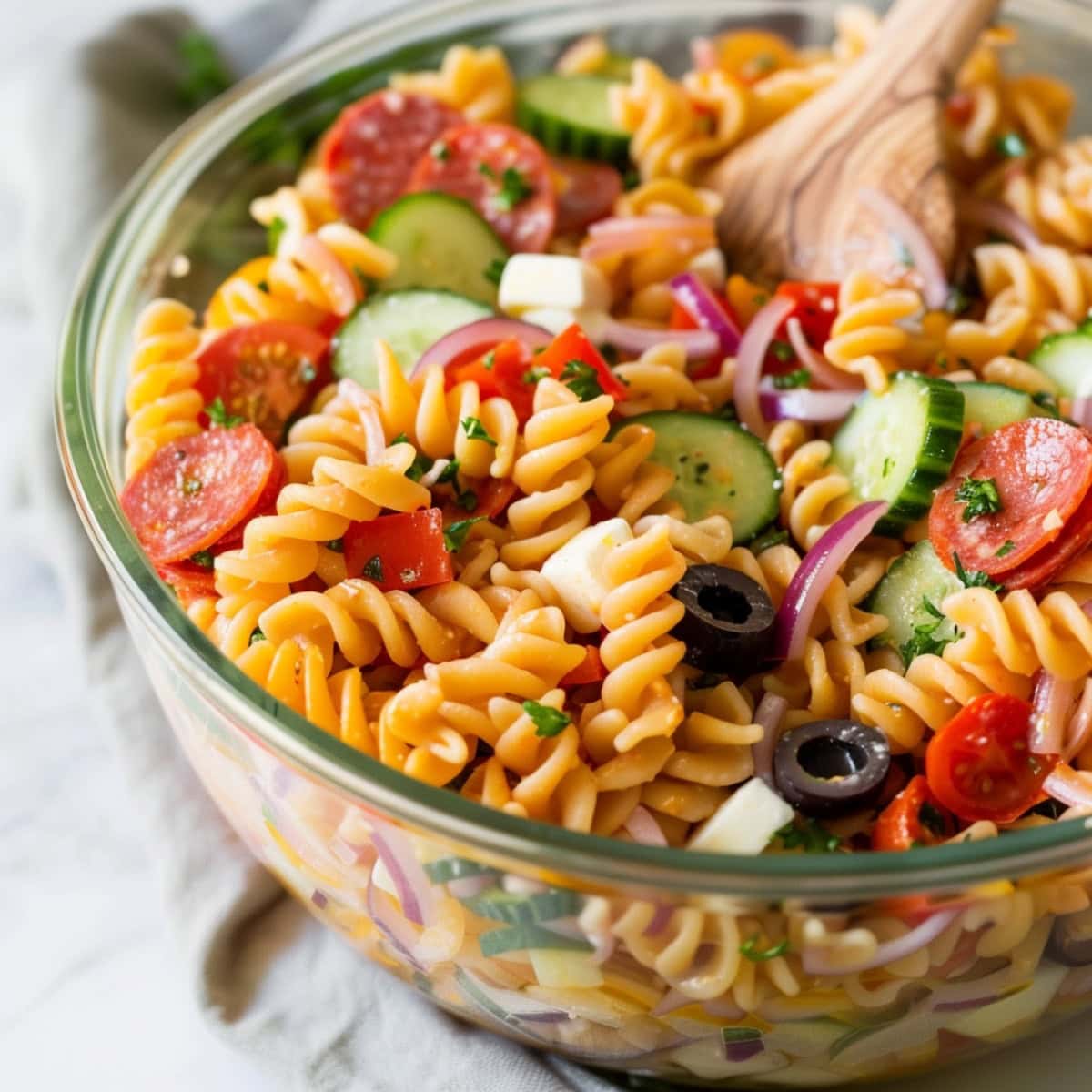 A glass bowl of supreme pasta salad with mozzarella, pepperoni and cucumbers.