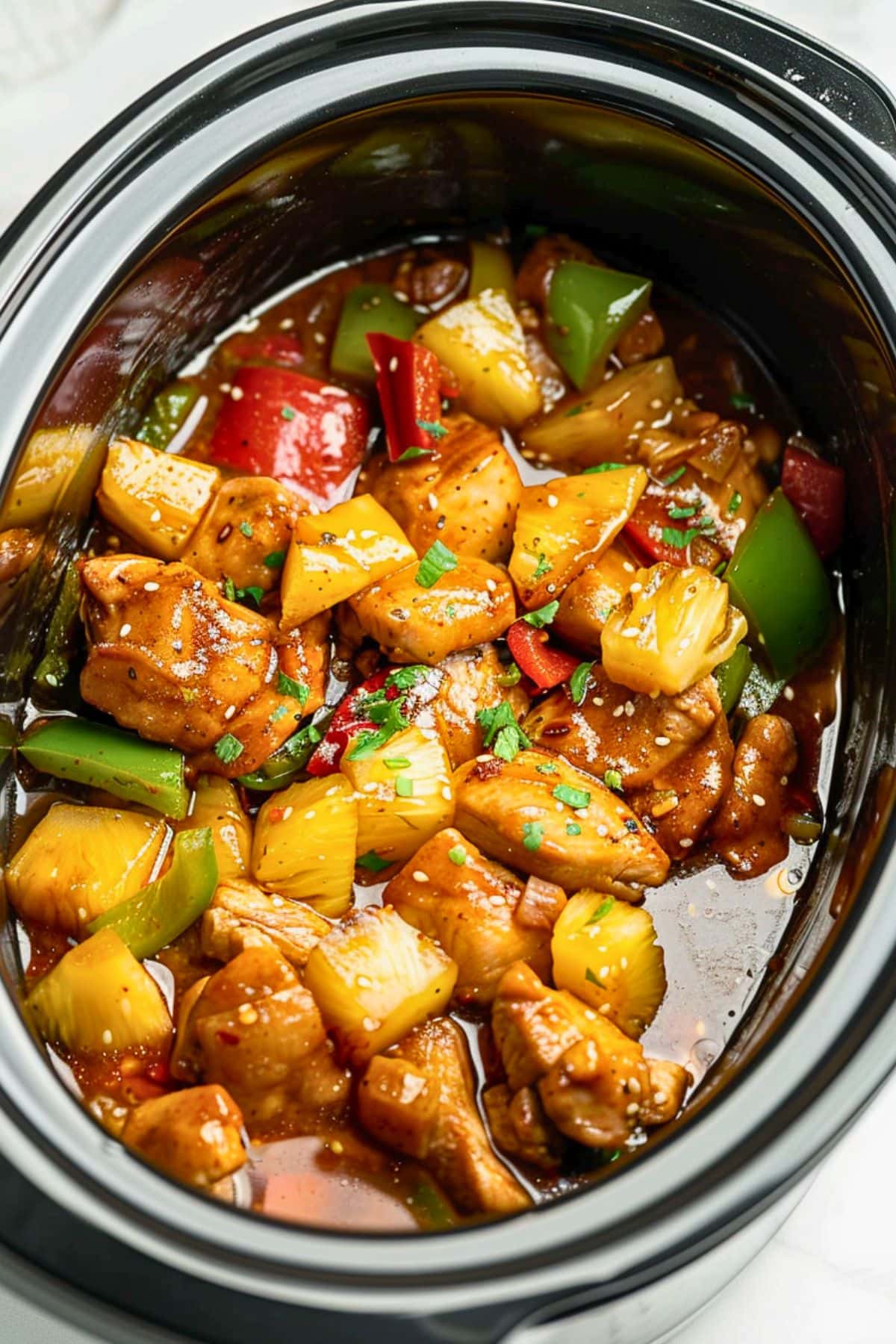 Pineapple chunks, green and red bell pepper, chicken thigh bite size cuts in soy sauce inside a slow cooker.