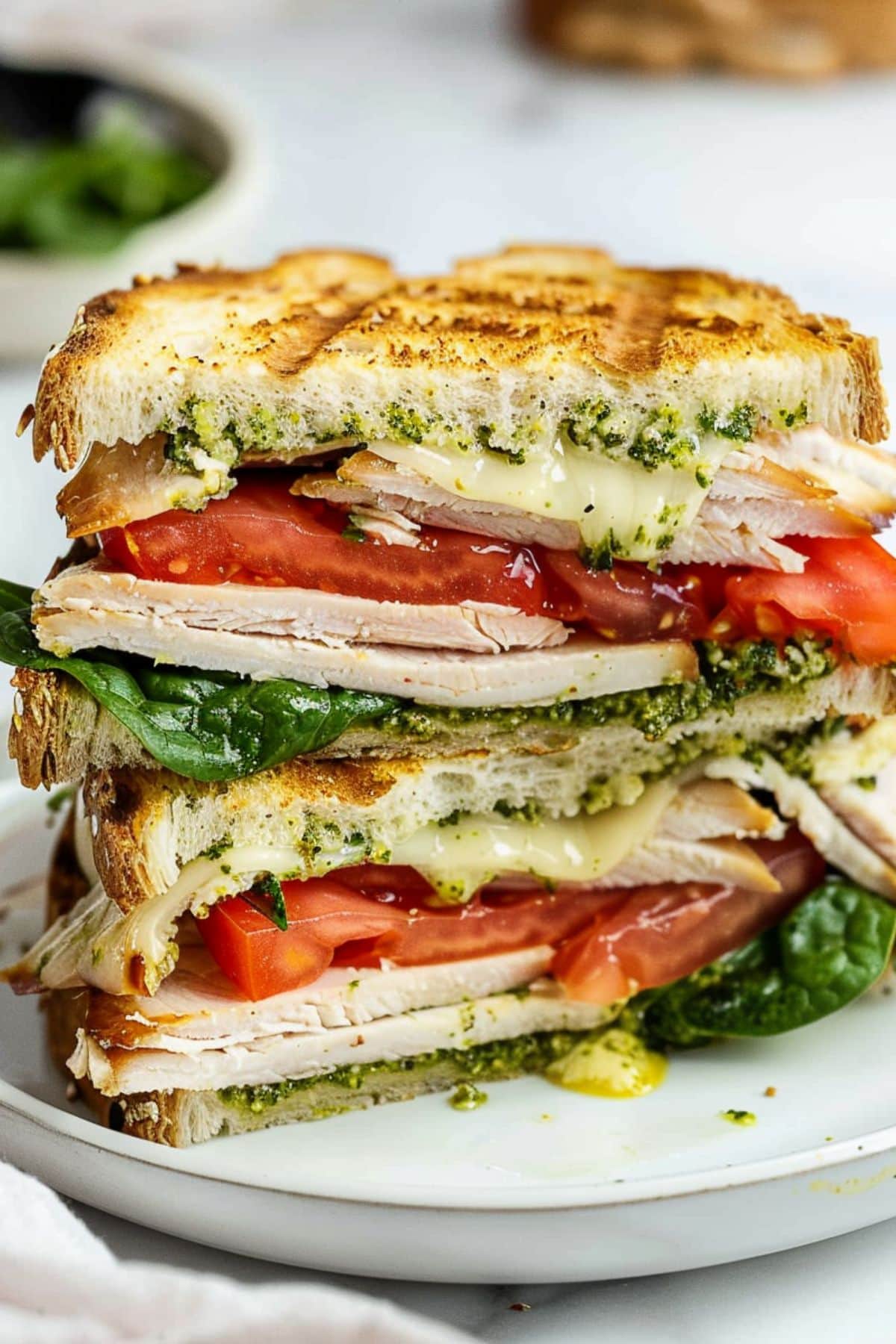 Sliced in half turkey pesto sandwich served on a white plate.