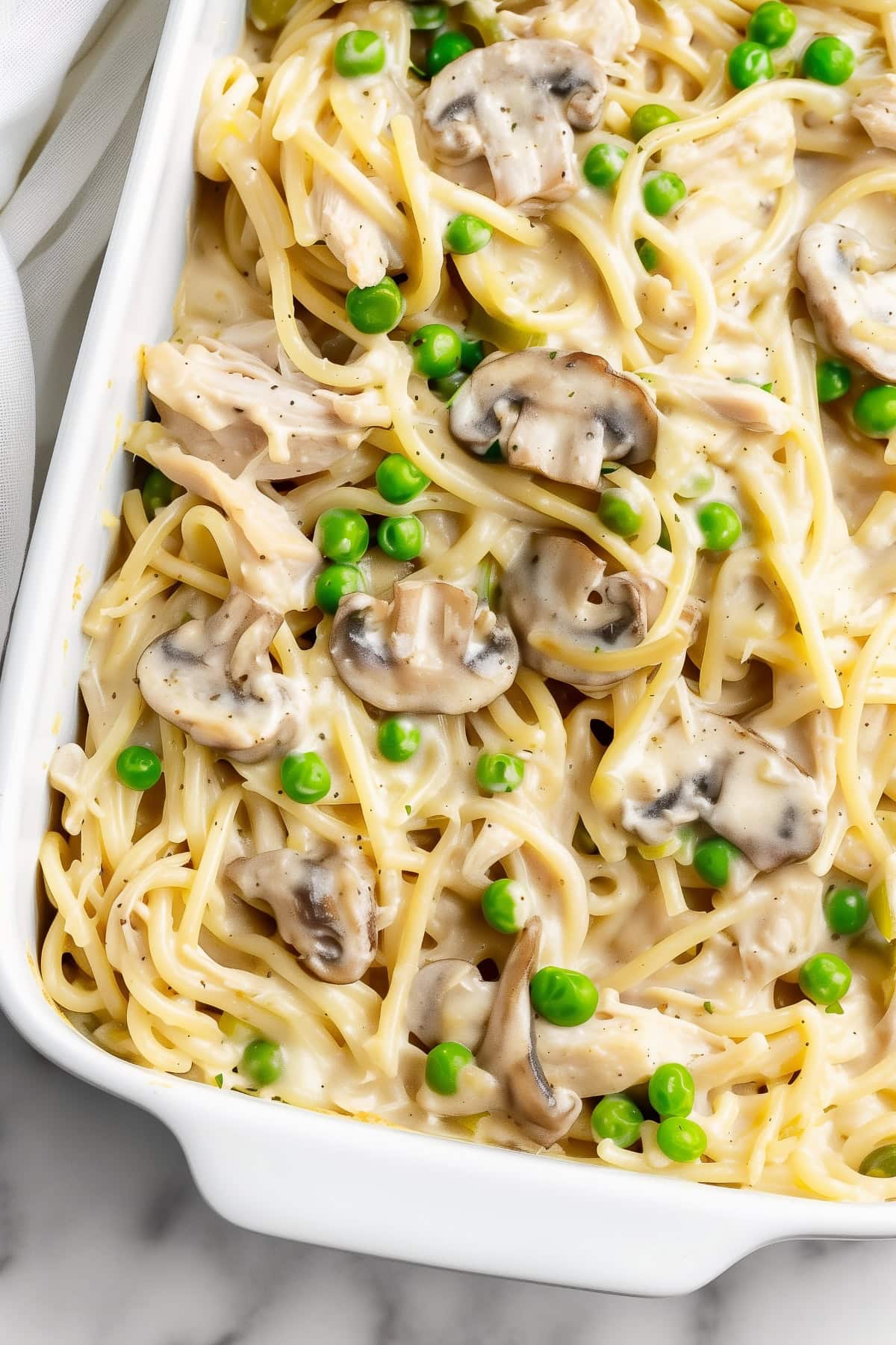 A white dish filled with turkey tetrazzini pasta with mushrooms and green peas.