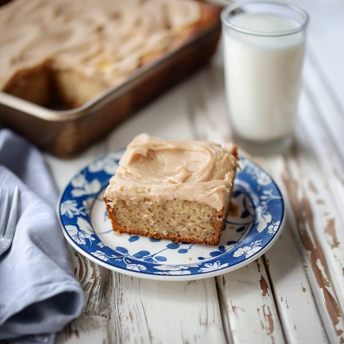 Banana Bread with Brown Butter Frosting slice served on a white blue plate, glass of milk next to it.