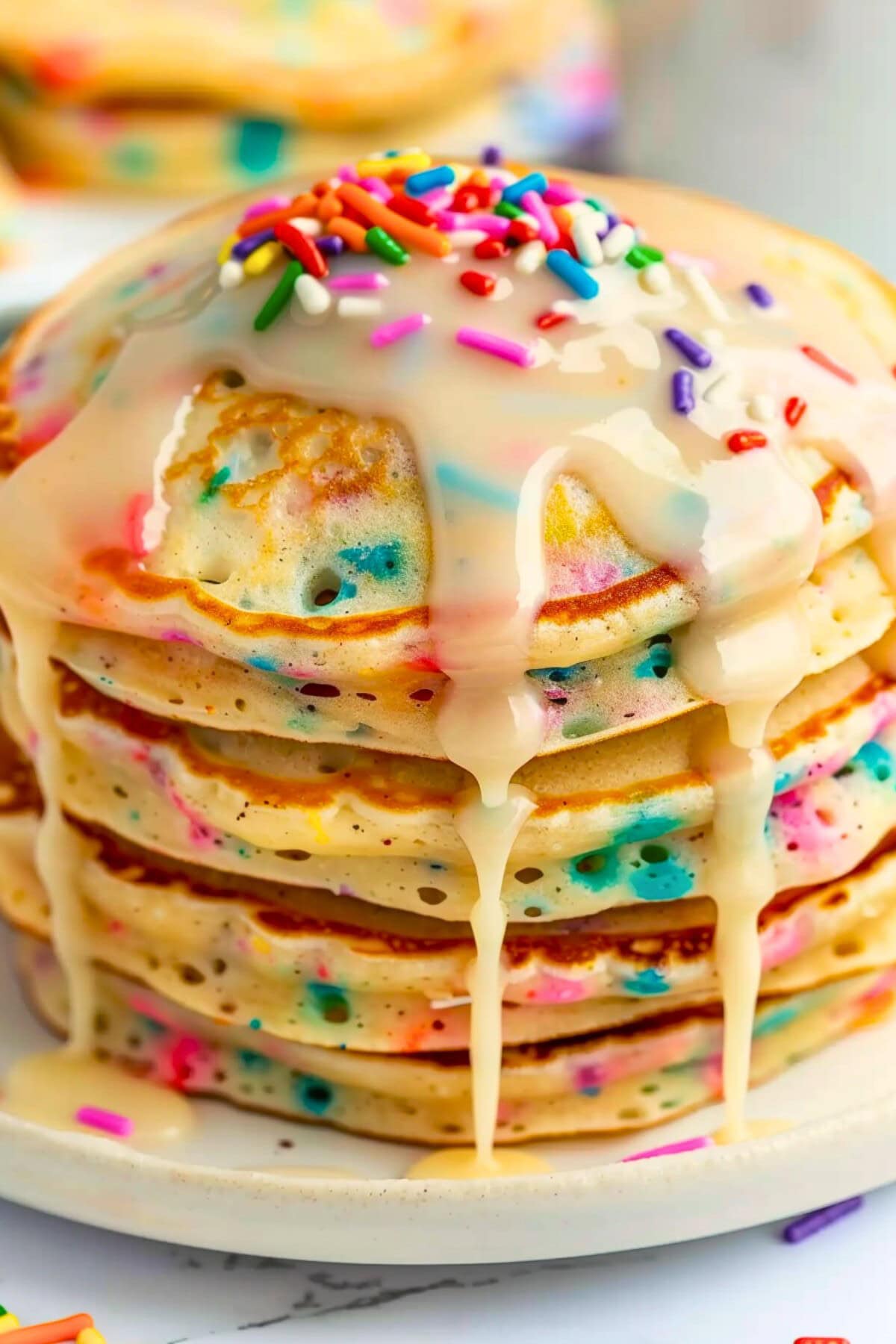 Stack of funfetti pancakes dripping with vanilla glaze sprinkled with candy sprinkles on top.