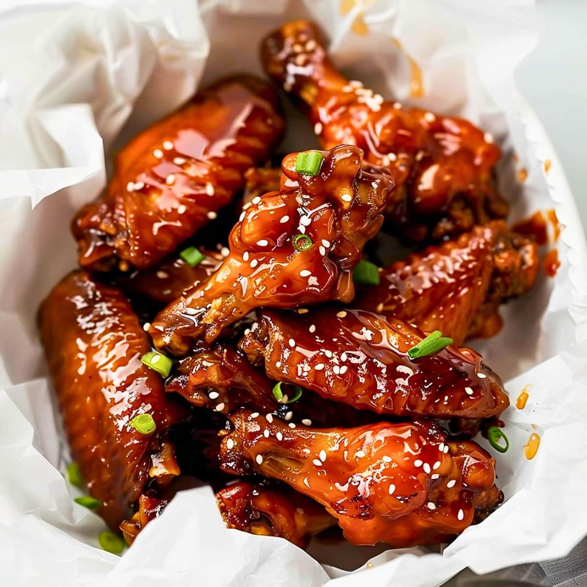 Bunch of honey glazed chicken wings served on a bowl with parchment paper.