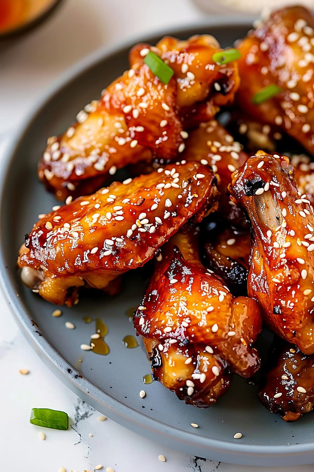 Chicken wings glazed with honey sprinkled with sesame seeds served on a gray plate.