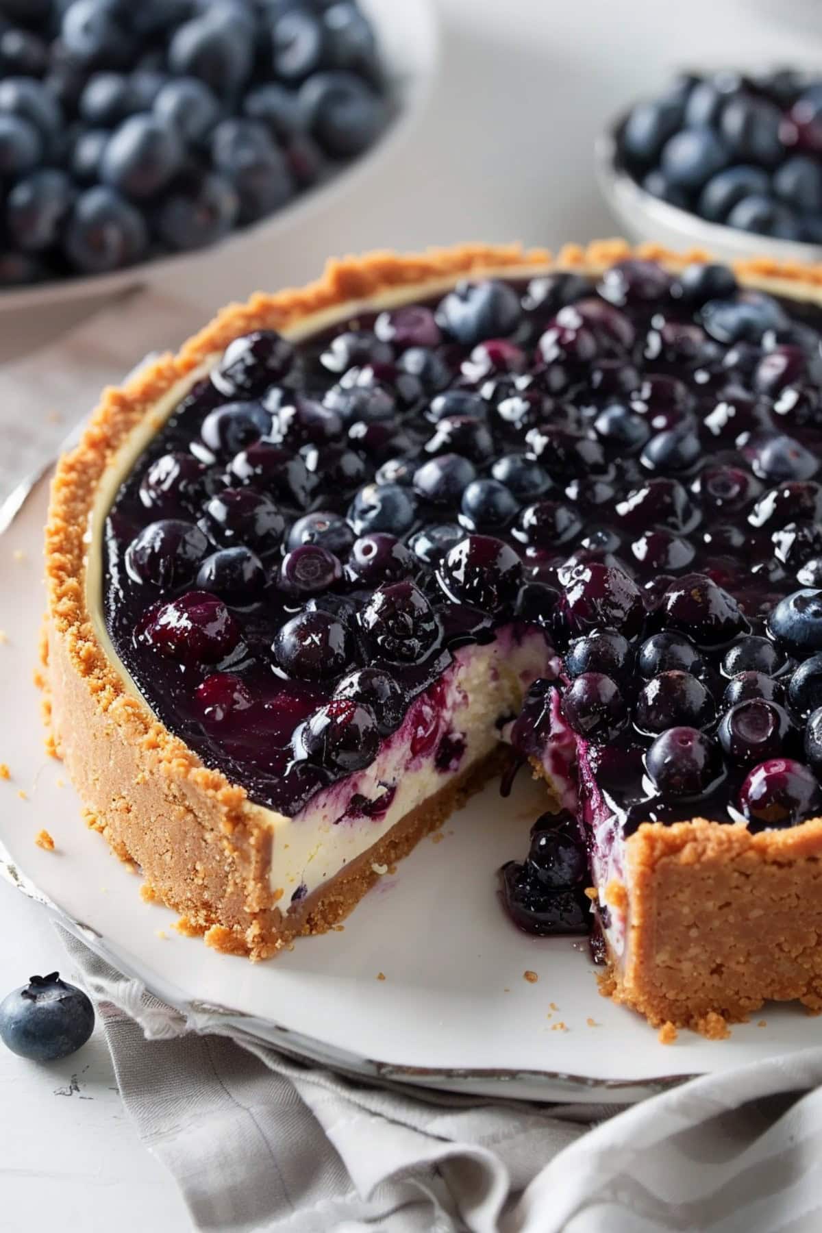 A whole blueberry lemon cheesecake on a serving plate with a slice removed.