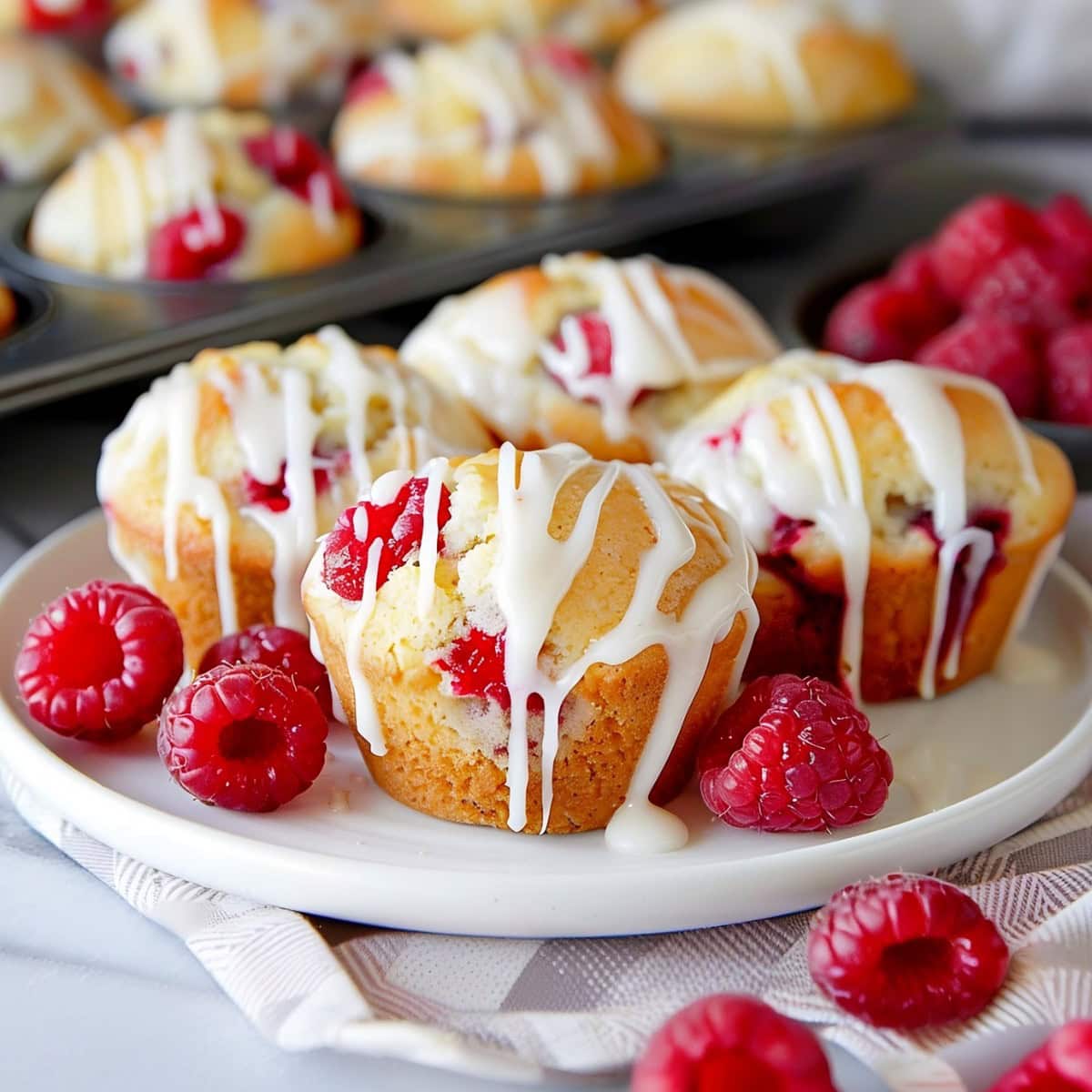 Four Lemon Raspberry Muffins with Glaze on a White Plate.