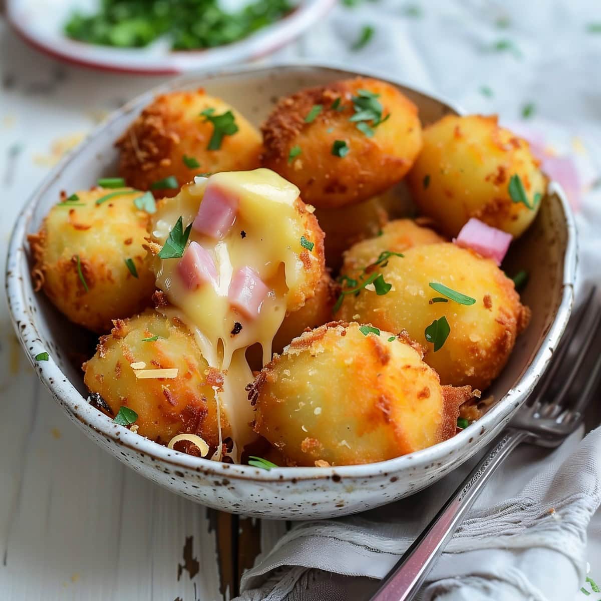 Potato croquettes in a white bowl, one piece sliced in half dripping in melted cheese.