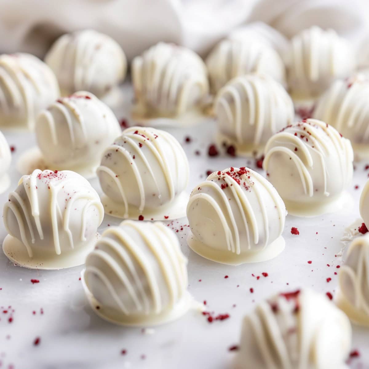 Red velvet cake truffles with white chocolate coating on a baking sheet with red velvet cake crumbs sprinkled on top