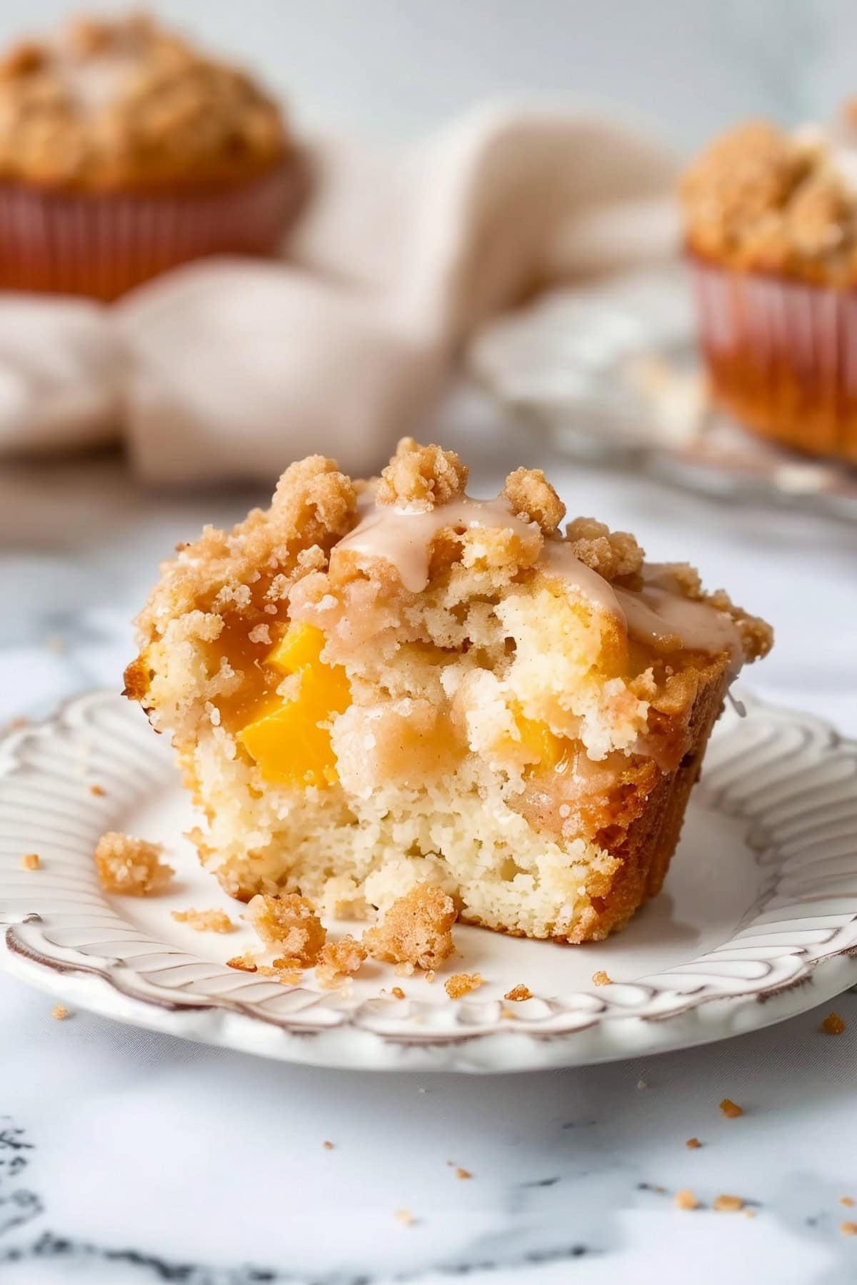 Golden peach streusel muffins with a crumbly topping, cut in half on a plate.