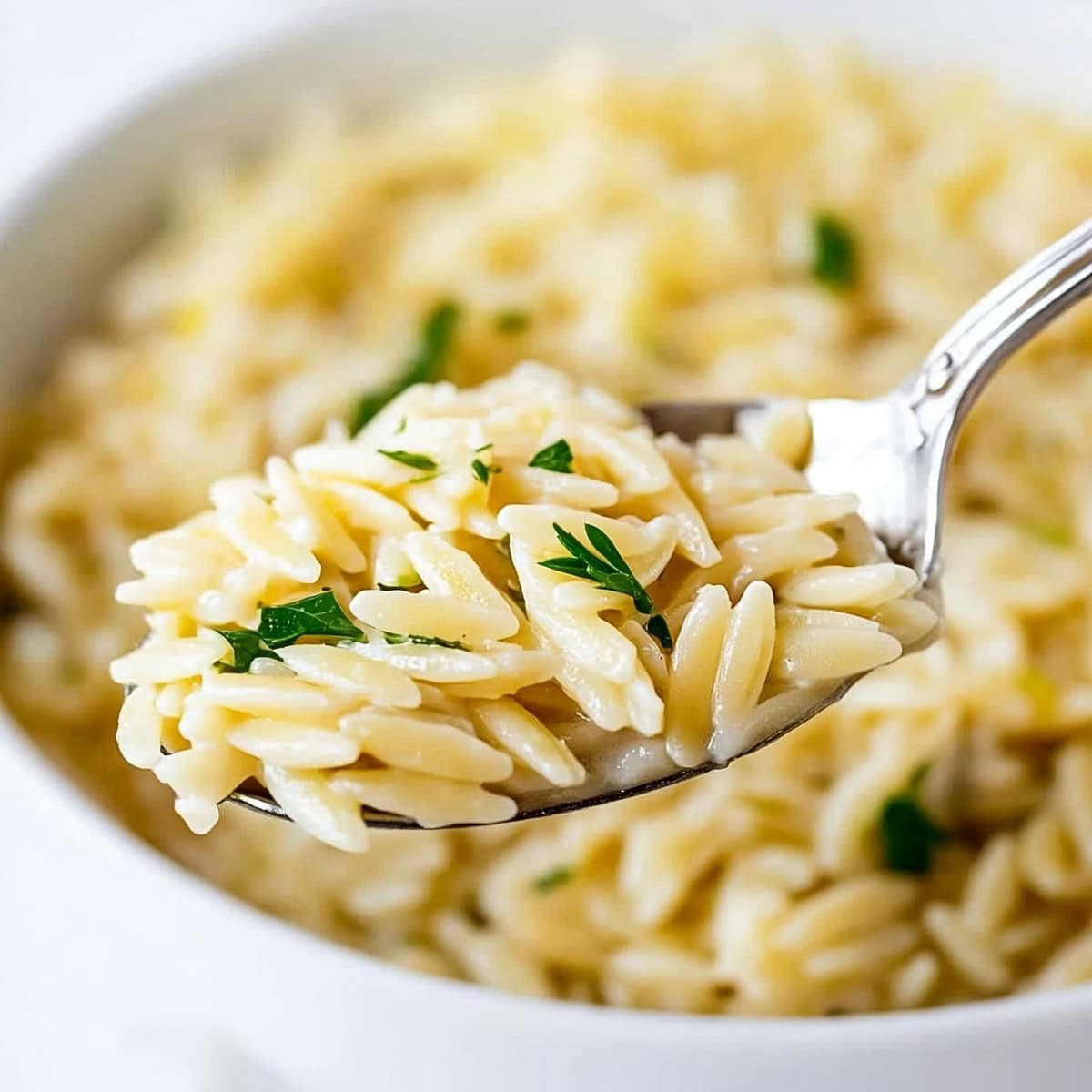 Close-up of lemon orzo garnished with fresh parsley in a spoon.