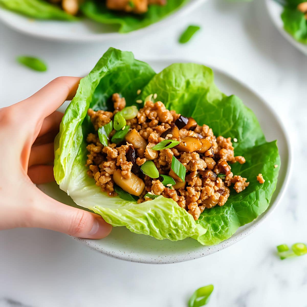 Hand holding lettuce wraps with ground chicken, chopped mushrooms and chestnuts filling.