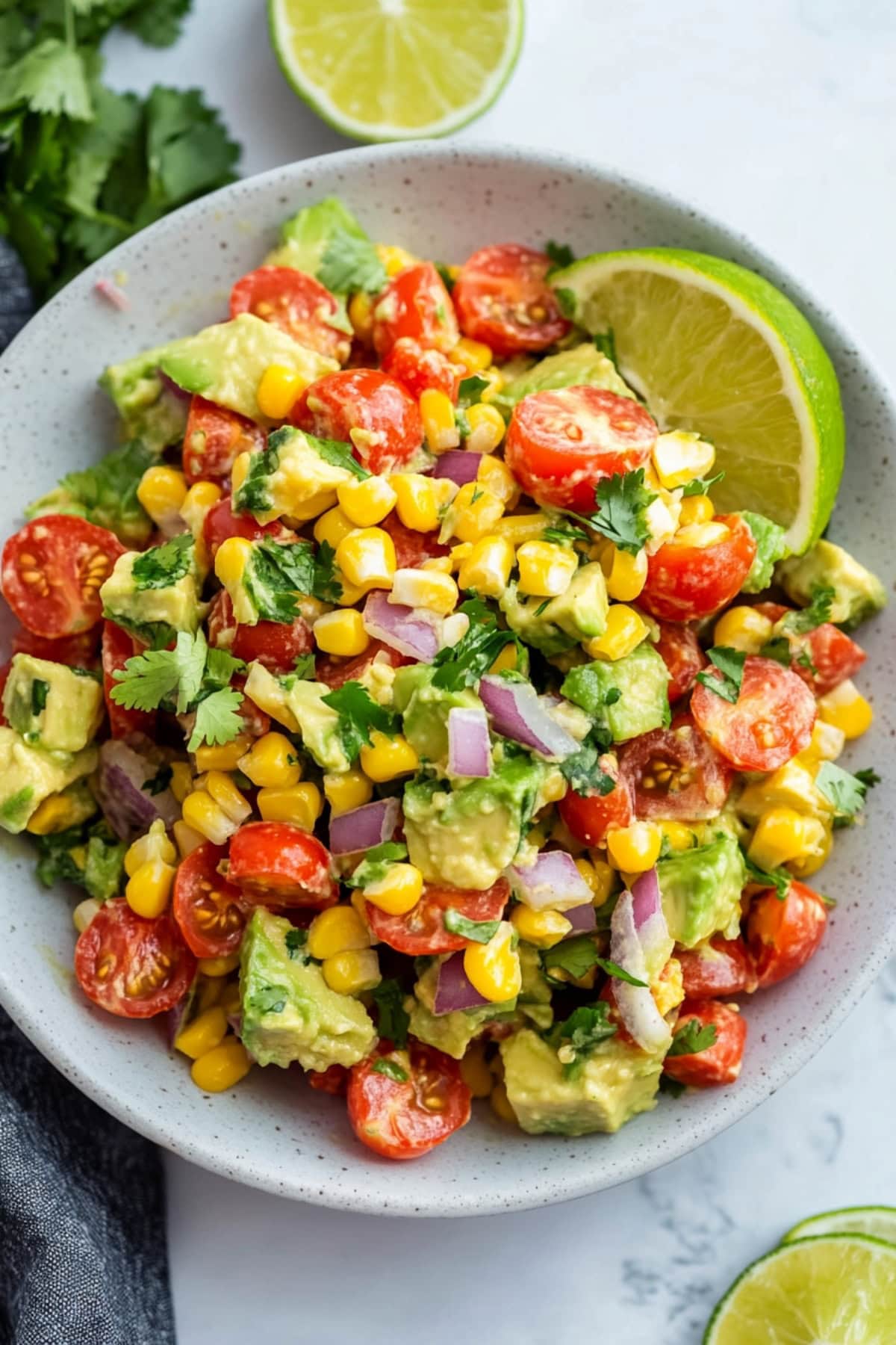 A serving of avocado corn salad with lime wedge on the side.