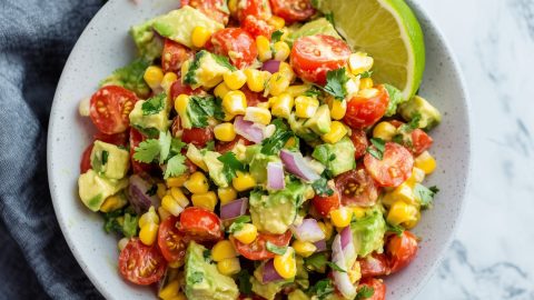 A colorful mix of avocado corn salad mixed with cherry tomatoes and red onions, garnished with chopped cilantro.