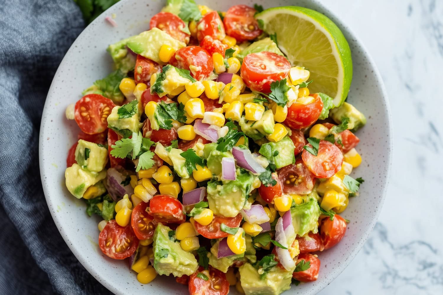 A colorful mix of avocado corn salad mixed with cherry tomatoes and red onions, garnished with chopped cilantro.