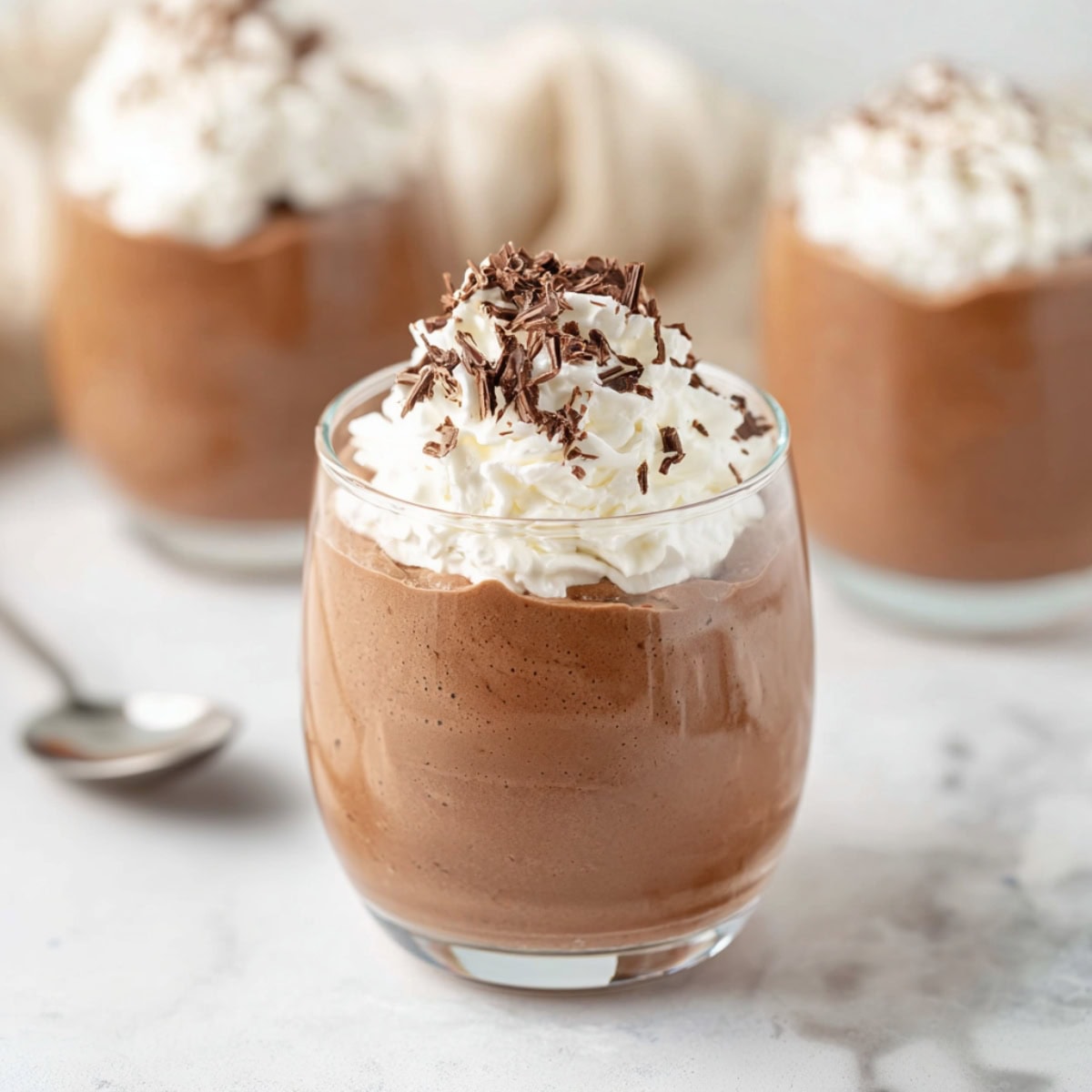 Creamy chocolate mousse in a clear glass with whipped cream on top.