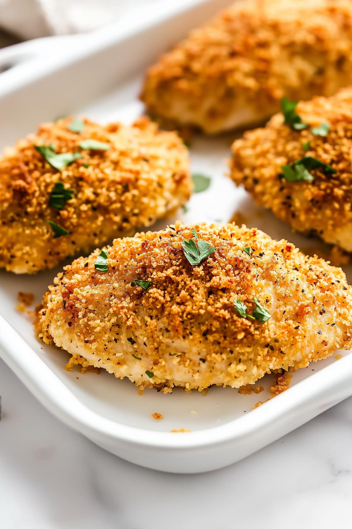 A baking dish filled with golden baked ranch chicken topped with fresh parsley.