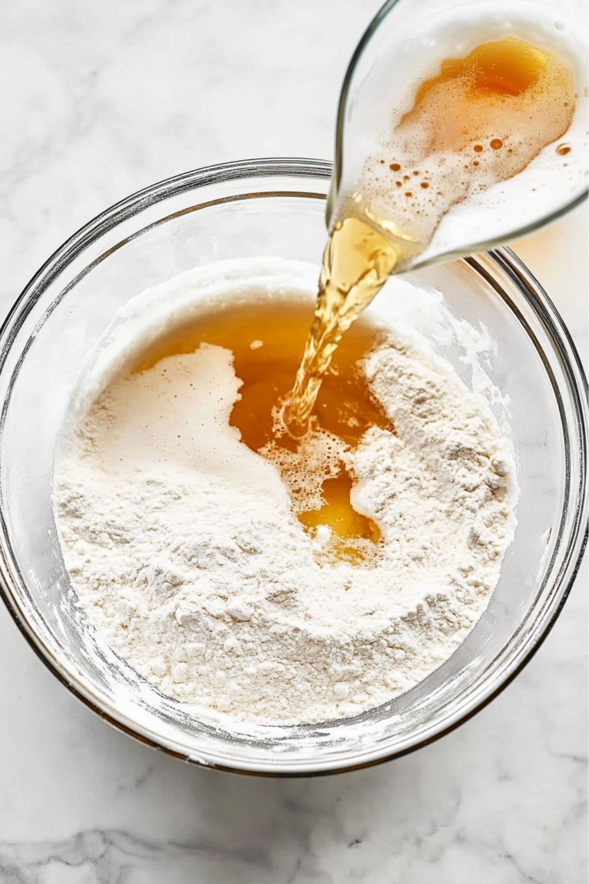 Beer poured over flour in a glass mixing bowl, top view