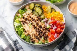 Big Mac bowl topped with shredded cheese, vegetables, and a generous dollop of special sauce.