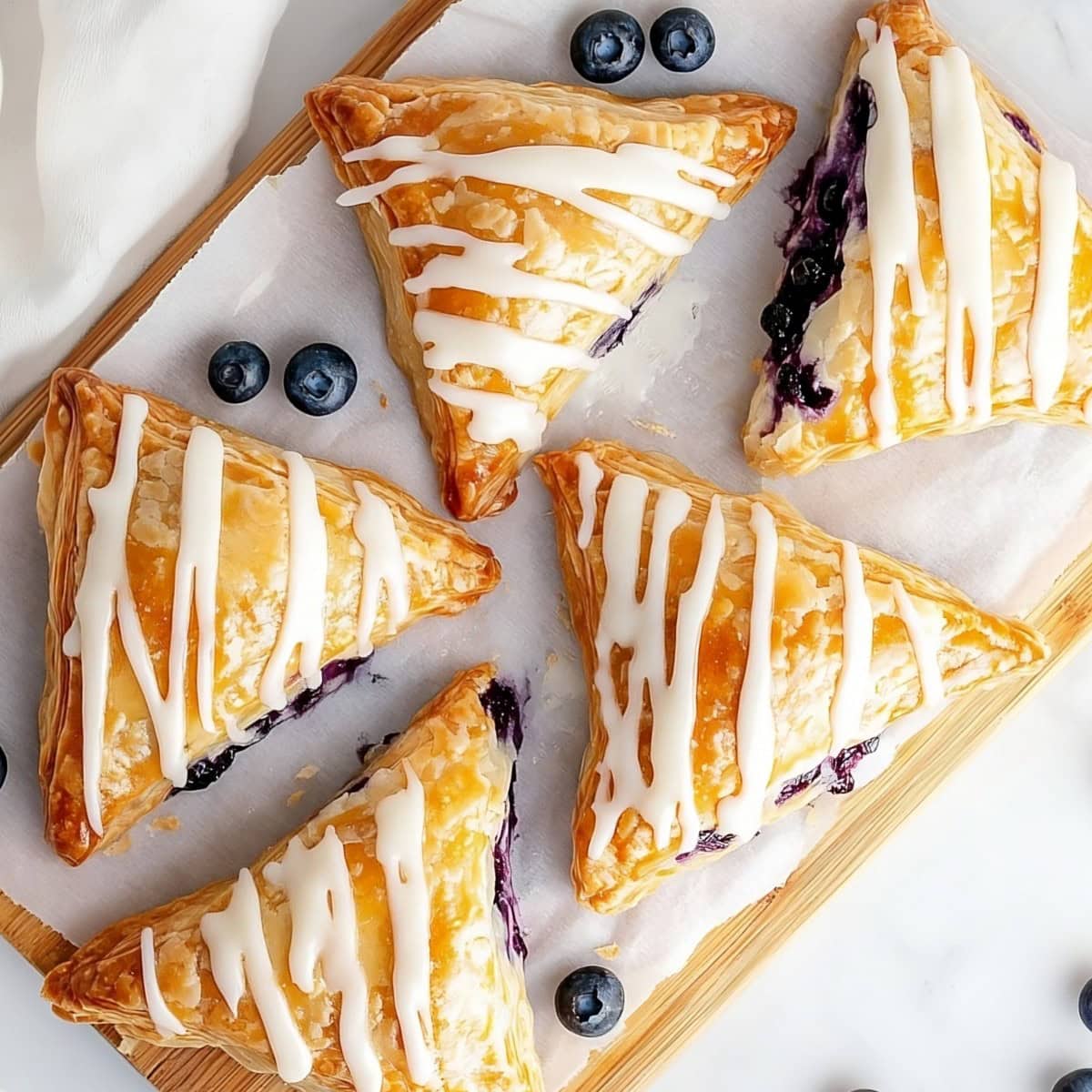 Blueberry turnovers drizzled with sweet glaze on a chopping board, top view