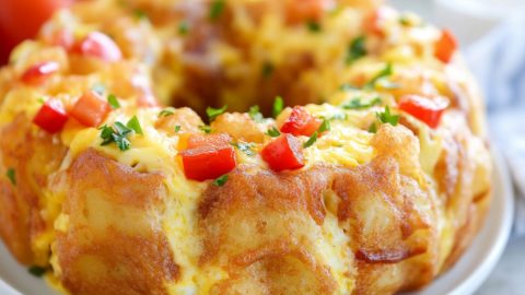 Breakfast bundt cake with diced peppers, onions hams and fluffy eggs served on a white plate.