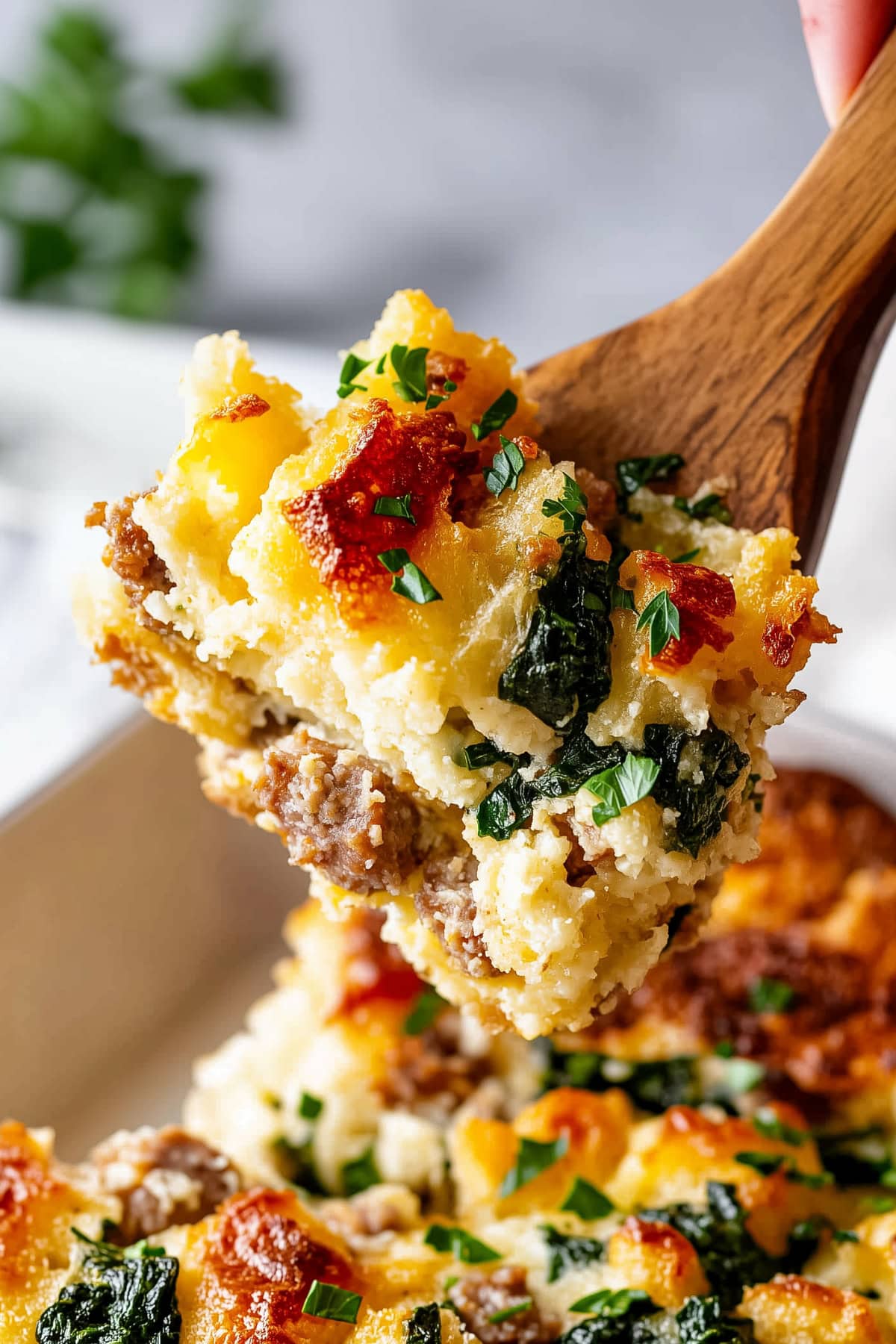 A piece of breakfast strata with sausage and spinach in a wooden spoon, close-up