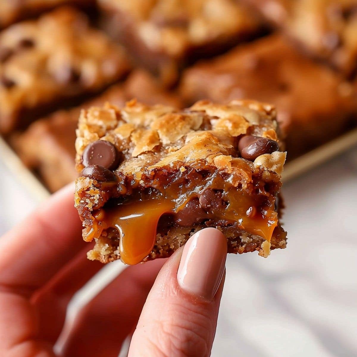 Hand holding a square slice of chocalatey carmelitas with gooey caramel. 