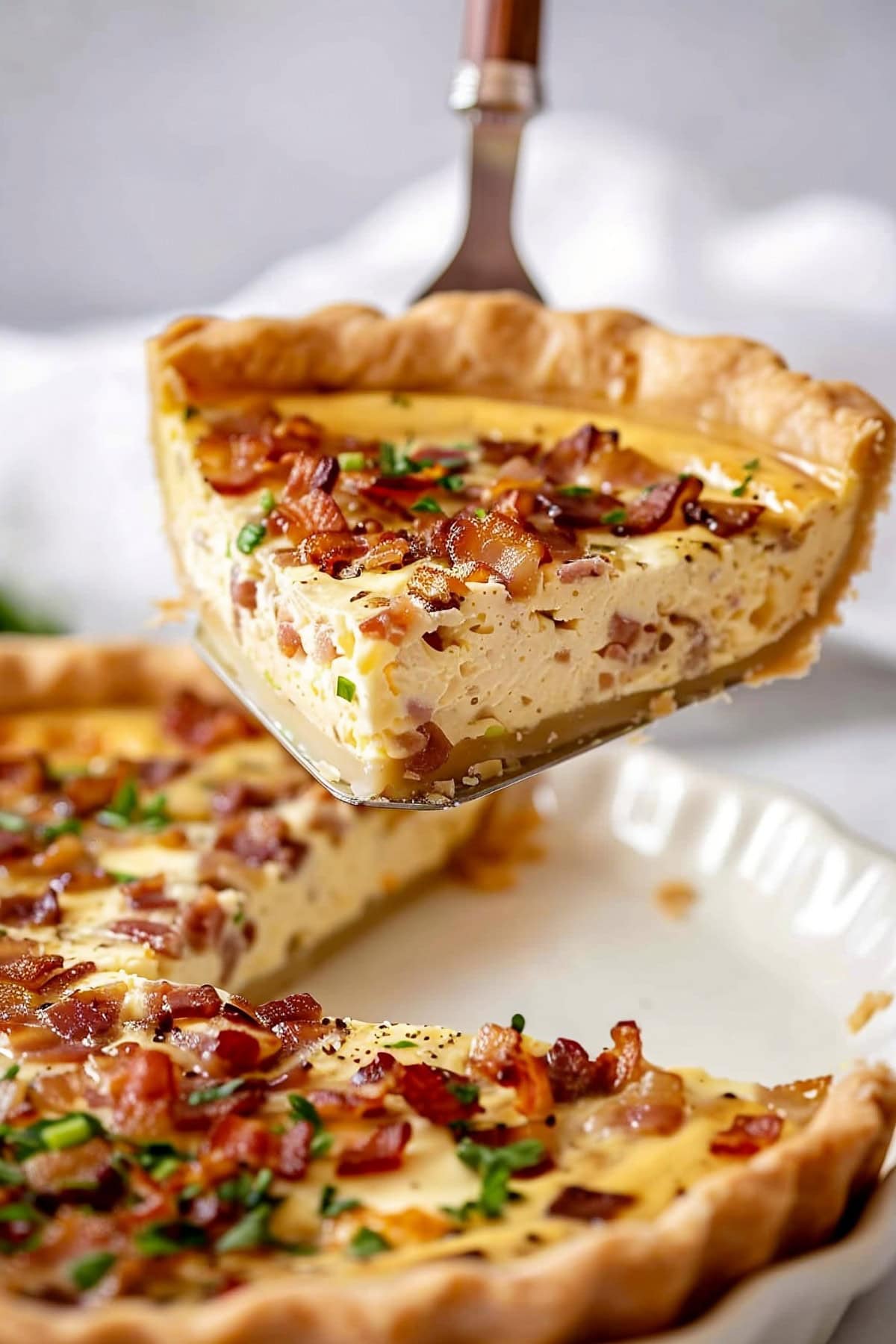 A pie spatula lifting a slice of Quiche Lorraine from a white white plate