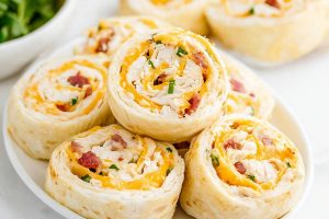 A plate of colorful chicken bacon ranch pinwheels with cheese, perfect for a party appetizer.