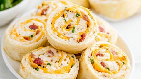 A plate of colorful chicken bacon ranch pinwheels with cheese, perfect for a party appetizer.