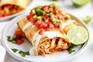 Sliced in half chicken chimichangas drizzled with white sauce and salsa served on a white plate.