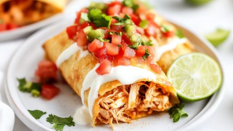 Sliced in half chicken chimichangas drizzled with white sauce and salsa served on a white plate.