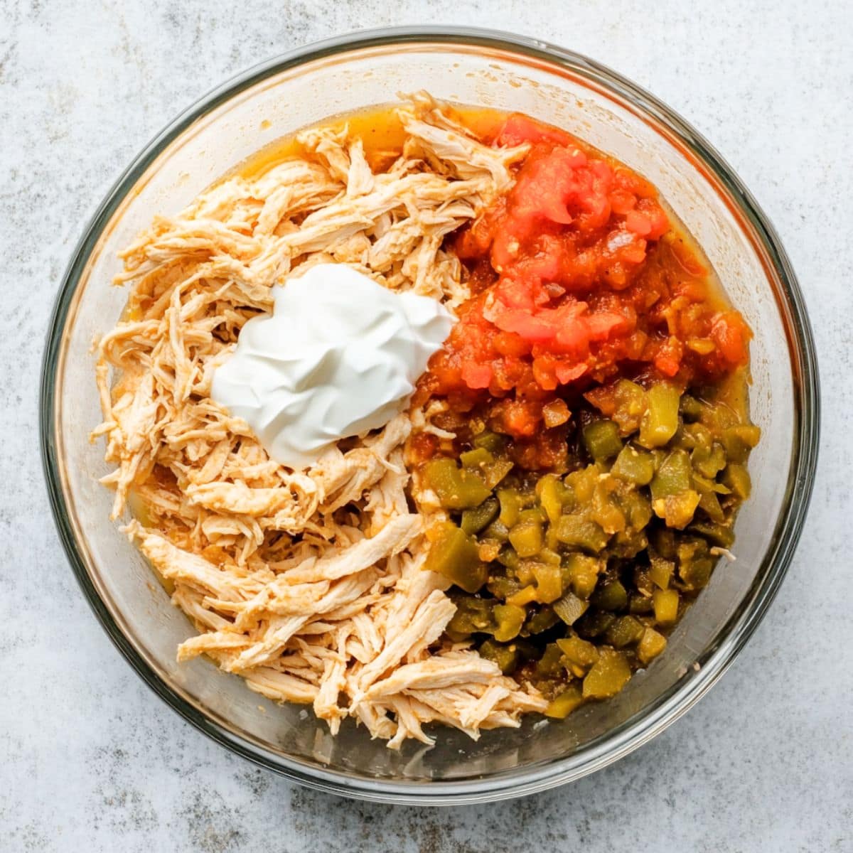 Shredded chicken, green chiles, salsa, and sour cream in a glass bowl, top view