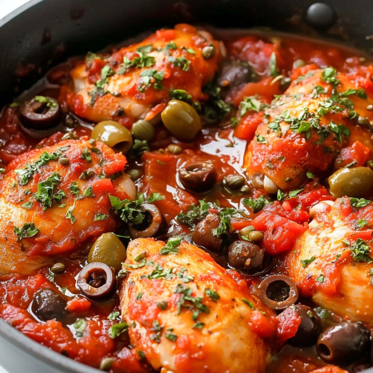 Chicken thigh cooked with olives, capers, anchovies and tomato sauce in a cast iron skillet.