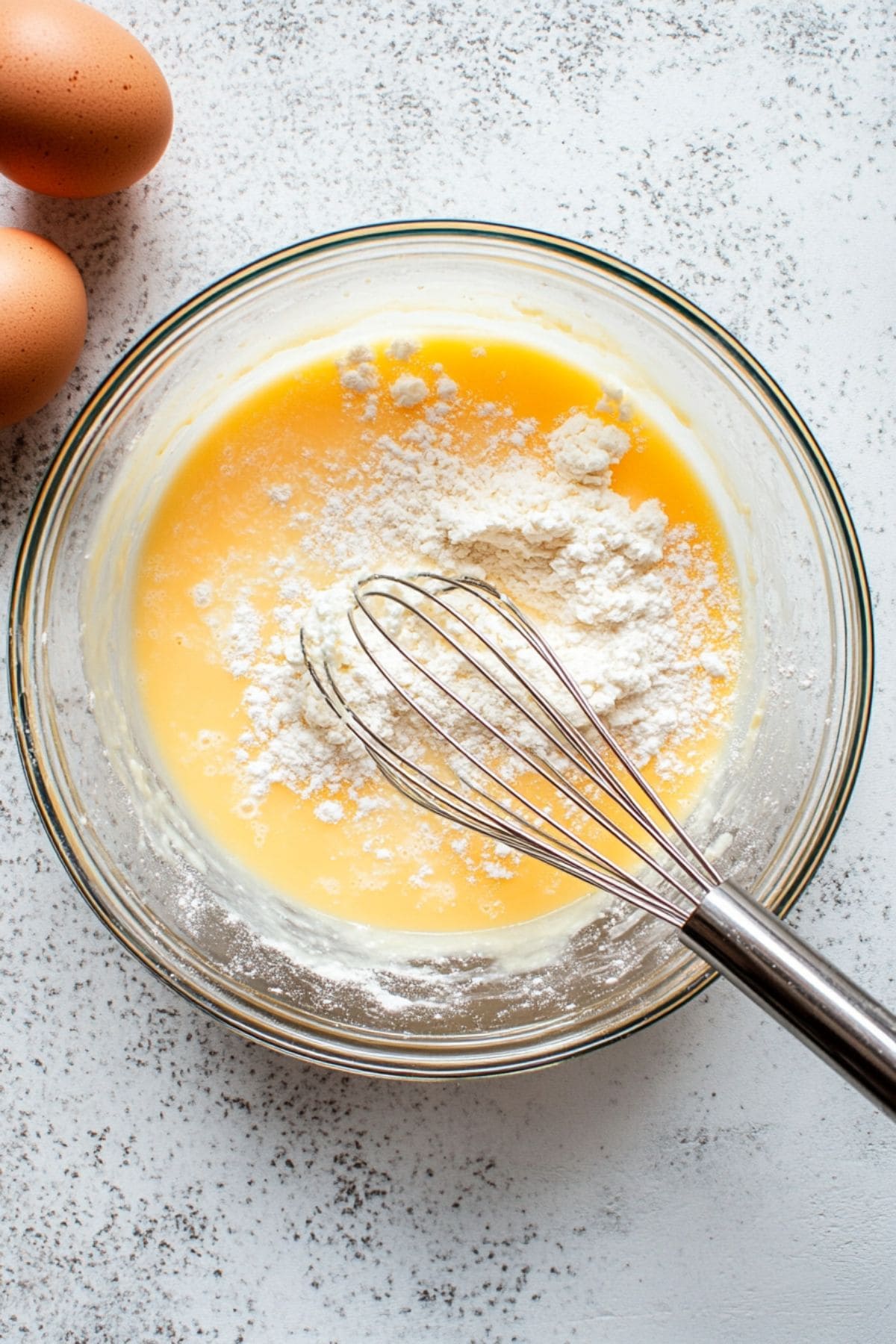 Egg and flour whisked in a glass mixing bowl, top view