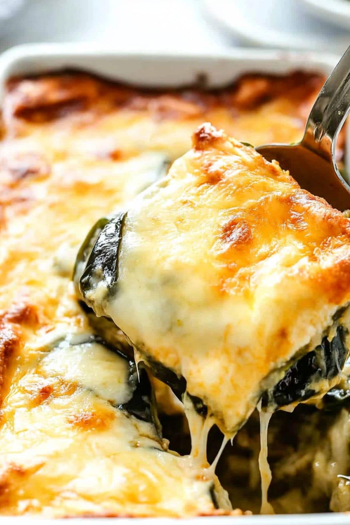 Metal spoon lifting a serving of cheesy chile relleno casserole from the dish, close up.