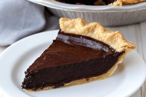 Slice of chocolatey fudge pie served in a white plate.