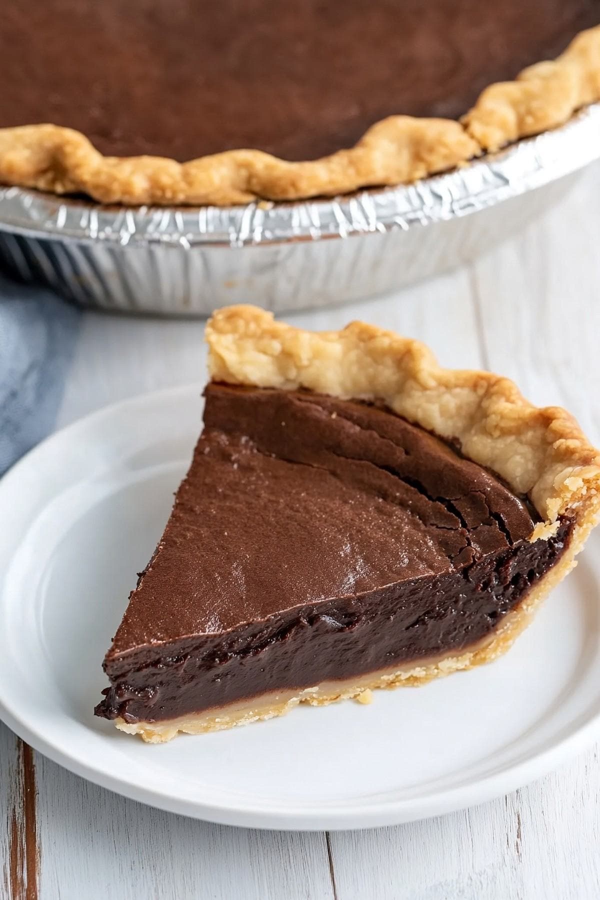 Chocolate fudge pie slice in a white plate with the rest of the pie in the background